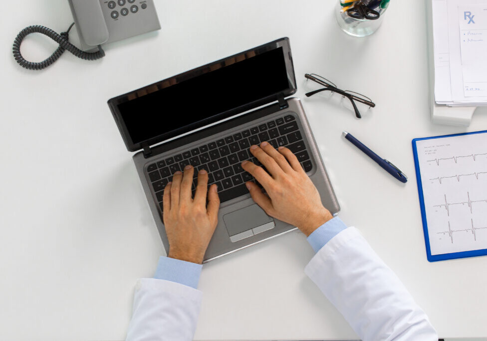 medicine, healthcare and people concept - doctor hands typing on laptop computer sitting at table in clinic